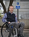 Photo of Chase Bearden in front of a handicap parking sign while sitting in his wheelchair