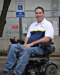 Photo of Mack Marsh in front of a handicap parking sign while sitting in his motorized wheelchair